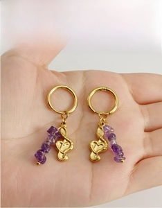 Macro shot of 18k gold music note earrings with purple amethyst stones held in hand