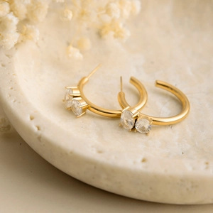 Macro view of gold-plated C-shaped earrings with inlaid oval zircon stones on ceramic tray