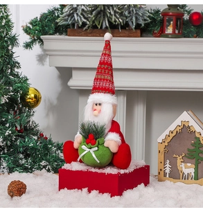 Detail of fabric Santa figurine with red pointed hat and green gift bag on snow base