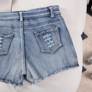 Close-up of distressed back pocket and frayed hem details on blue denim shorts