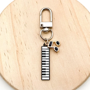 Detail of musical piano and note charms on a silver keychain over a wooden background