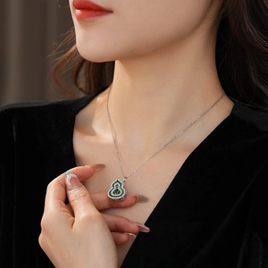 Detailed view of an emerald zircon gourd pendant necklace on a silver chain worn by a model