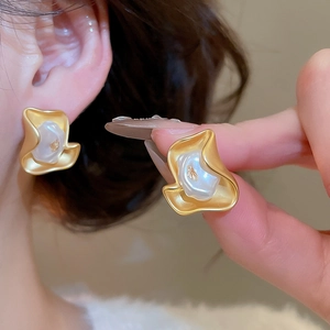 Close-up of matte gold wavy flower earrings with pearl centers on an ear model