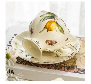 Detailed view of ceramic cup and saucer with lemon and butterfly patterns and gold rim