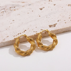 Macro detail of 18K gold-plated twisted rope hoop earrings on a beige stone surface
