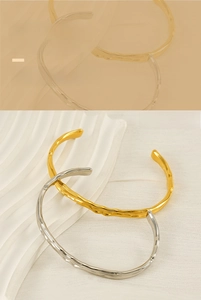 Dettaglio della trama martellata sui bracciali aperti in acciaio al titanio placcati oro e argento