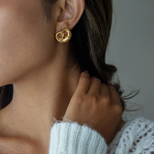 Close-up of a model wearing a large 18K gold-plated stainless steel pretzel heart earring