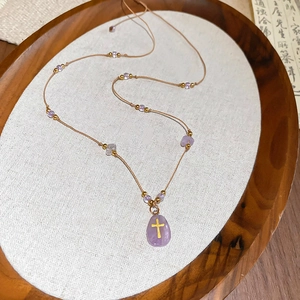 Détail du pendentif en pierre violette avec croix dorée sur fond de lin