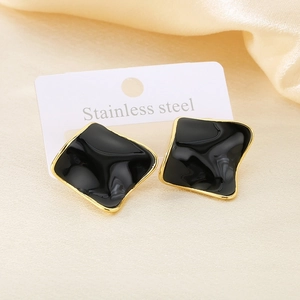 Detailed close-up of geometric black and gold stainless steel earrings on silk