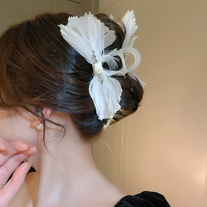 Detailed view of elegant white feather hair claw with rhinestones in a sleek updo hairstyle