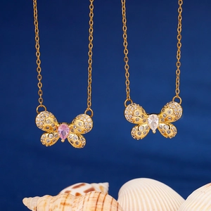 Golden butterfly necklace with pink and white zircon stones on dark blue background