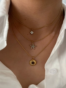 Close-up of a layered gold necklace with floral, starfish and sunburst pendants on white shirt