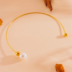 Vue détaillée du collier ras de cou en perles dorées sur une surface texturée chaleureuse
