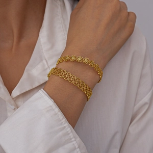 Detail of gold floral and geometric hollow cuff bracelets on a model's wrist