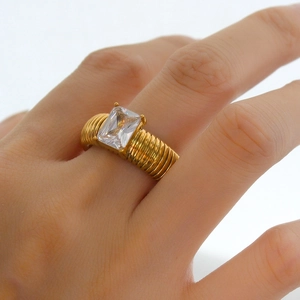 Gold ribbed band ring with rectangular clear crystal stone shown on a model's finger