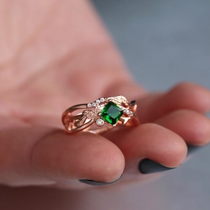 Detailopname van roségouden ring met vierkante groene zirkoon en elegante ranken