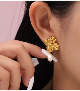 Close-up of golden flower earrings with white teardrop pearls on a model