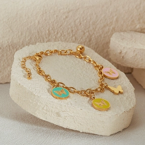 Gold chain bracelet with colorful enamel butterfly charms on a white stone background