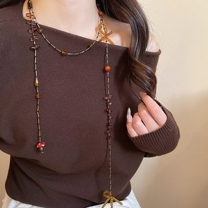 Detail of beaded bow necklace with amber beads and small mushroom charm on a sweater