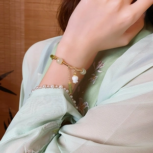 Détail d'un bracelet doré style bambou avec perles de jade et breloque muguet