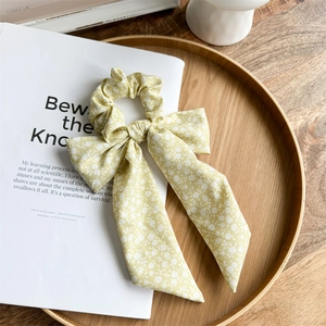 Close-up of a floral bow scrunchie with ribbons on a wooden tray and magazine