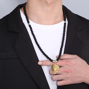 Close-up of men's black bead necklace with gold lion head pendant on a male model