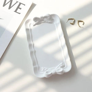 Flat lay of white bowknot plaster jewelry tray with elegant shutter shadows