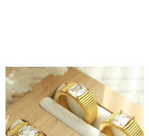 Detalle de anillos dorados con circonitas rectangulares y relieve vertical en soporte madera