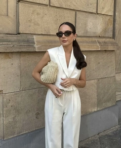 Detail of white sleeveless suit vest paired with wide-leg trousers and a straw clutch
