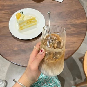 Close-up of hand holding a ribbed glass cup with iced coffee on a wooden table