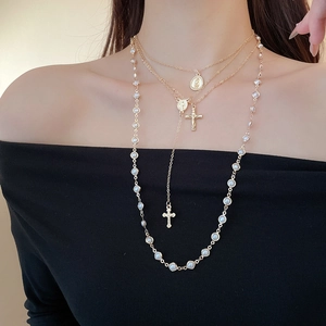 Close-up of layered gold necklace with cross pendant, coin medallion and pearls