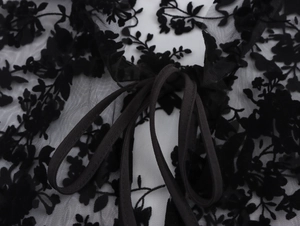 Close-up of black mesh fabric with floral embroidery and lace-up tie details on a blouse