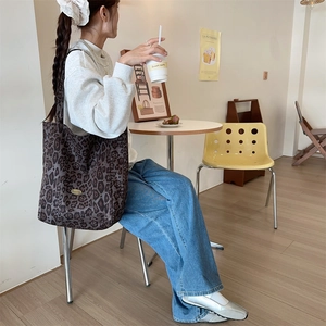 Close-up of leopard print canvas tote bag carried by a model in a cozy cafe setting