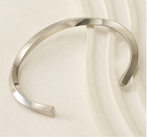 Macro shot of silver-tone C-shape twisted bangle showing mirror-polished steel surface