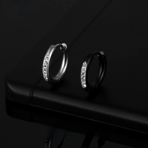 Close-up of silver and black stainless steel huggie earrings with a single row of crystals