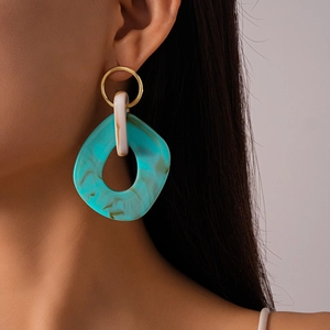 Close-up of oversized geometric resin earrings with green marble texture and gold finish