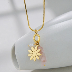 Detail view of golden necklace with floral charm, white pearl, and pink stone accents