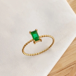 Macro shot of a twisted gold band ring featuring a rectangle emerald green stone