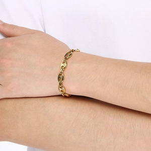 Close-up of golden mariner link chain bracelet worn on wrist over a white t-shirt