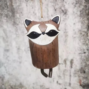 Detail view of a rustic raccoon wind chime hanging by a rope against a stone wall