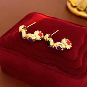 Macro detail of vintage gold C-shaped earrings with red, green and purple gems on velvet