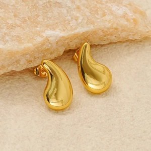 Chic golden comma teardrop earrings with polished finish on a stone texture background