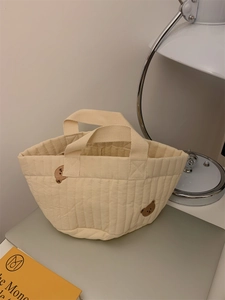 Detail of quilted beige fabric bag featuring brown bear embroidery and soft textured handle