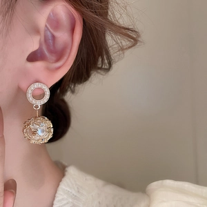 Detail view of hollow gold mesh ball earrings with pearls worn by a model in soft lighting