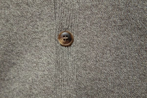 Macro shot of grey knitted sweater texture with a brown wood-pattern button detail