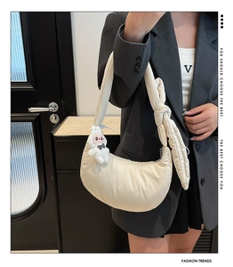 Détail d'un sac croissant rembourré crème avec bandoulière nouée et breloque lapin
