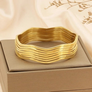 Set of seven wave-shaped gold stainless steel bangles stacked on a jewelry box