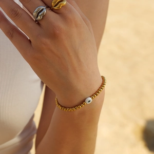 Bracelet œil porte-bonheur plaqué or 18k et bagues lèvres sur fond de plage