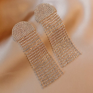 Macro detail of golden U-shaped rhinestone fringe earrings on champagne silk fabric
