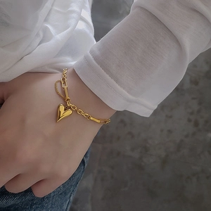 Detailed macro of a 18k gold double-layered chain bracelet with a polished heart pendant
